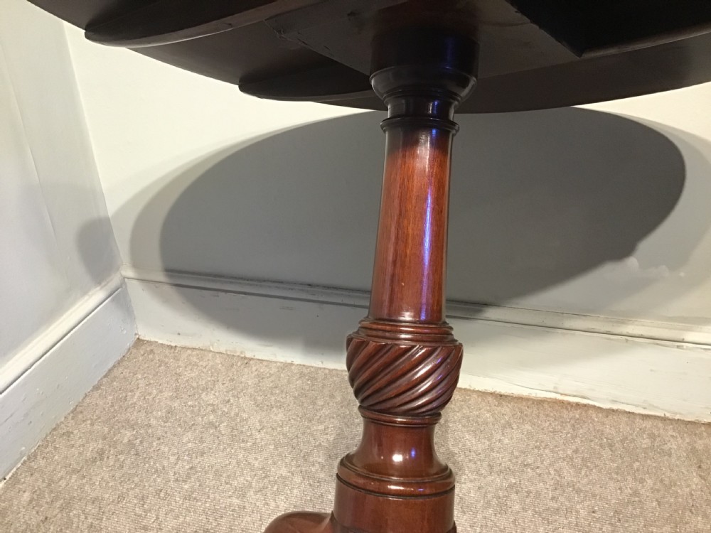 A dark mahogany circular tripod table with a turned central column featuring spiral carving and three cabriole legs with pad feet. View V