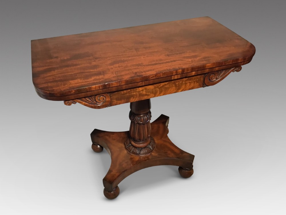 A Regency period flame mahogany fold-over card table featuring a carved pedestal column, a quadruped platform base, and scroll corner brackets.