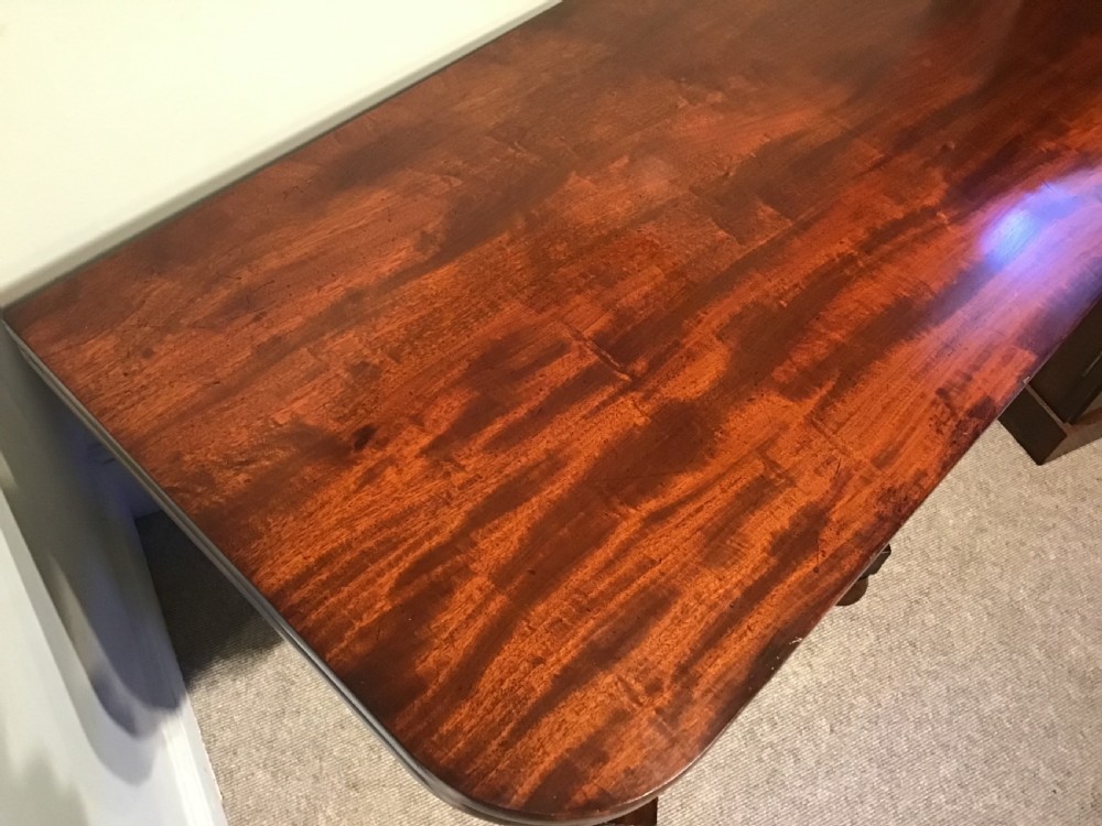 A Regency period flame mahogany fold-over card table featuring a carved pedestal column, a quadruped platform base, and scroll corner brackets. View V