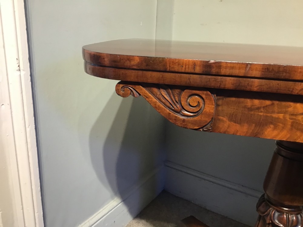 A Regency period flame mahogany fold-over card table featuring a carved pedestal column, a quadruped platform base, and scroll corner brackets. View VI