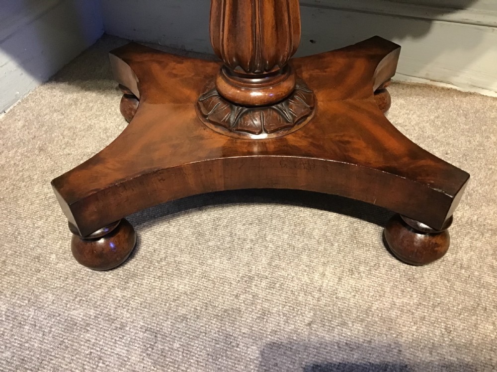 A Regency period flame mahogany fold-over card table featuring a carved pedestal column, a quadruped platform base, and scroll corner brackets. View IX
