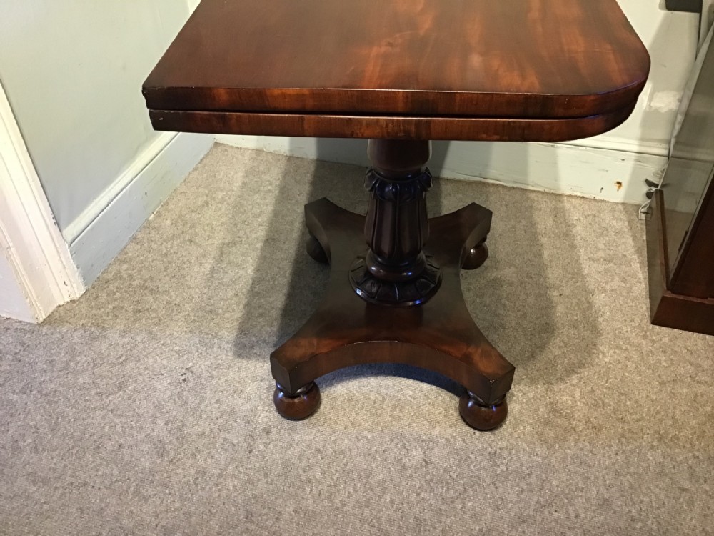 A Regency period flame mahogany fold-over card table featuring a carved pedestal column, a quadruped platform base, and scroll corner brackets. View X