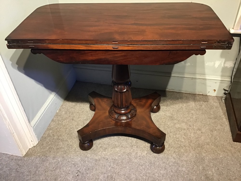 A Regency period flame mahogany fold-over card table featuring a carved pedestal column, a quadruped platform base, and scroll corner brackets. View XI