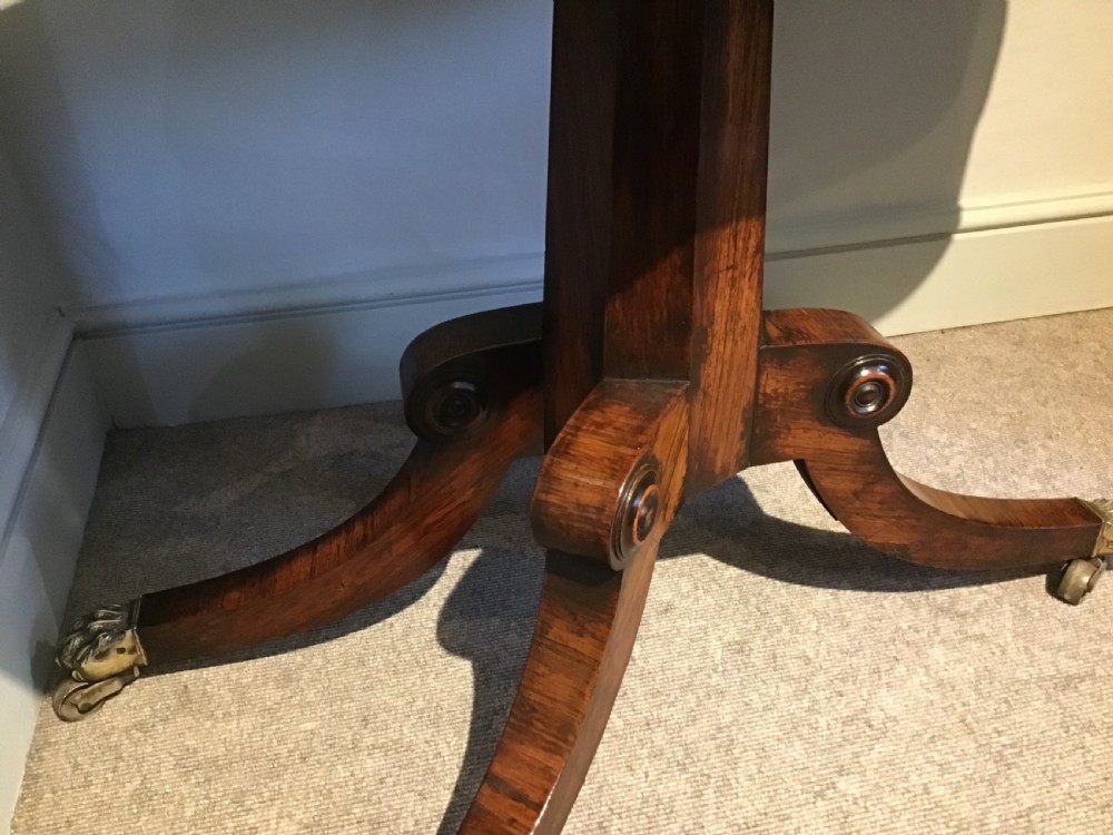 A Regency rosewood card table featuring a rectangular swivel top with rounded corners, supported by a central pedestal column and splayed legs ending in brass lions paw castors. View IV