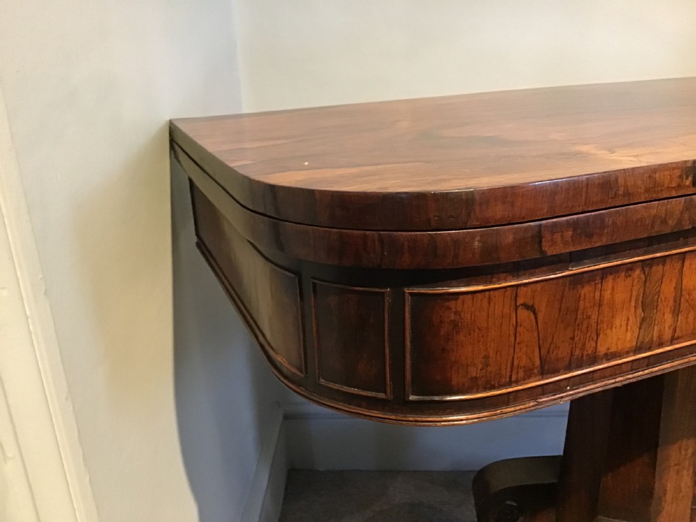 A Regency rosewood card table featuring a rectangular swivel top with rounded corners, supported by a central pedestal column and splayed legs ending in brass lions paw castors. View VI