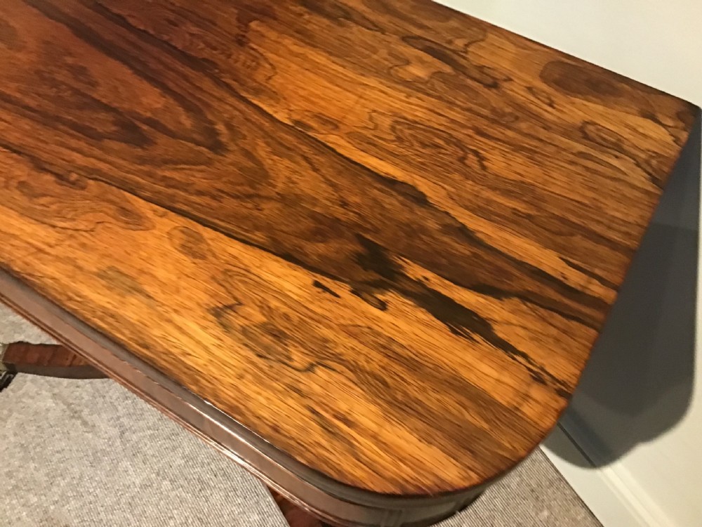 A Regency rosewood card table featuring a rectangular swivel top with rounded corners, supported by a central pedestal column and splayed legs ending in brass lions paw castors. View VII