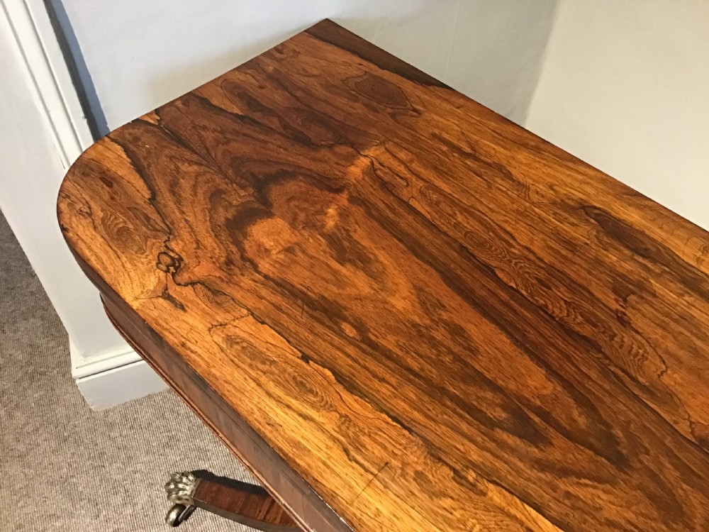 A Regency rosewood card table featuring a rectangular swivel top with rounded corners, supported by a central pedestal column and splayed legs ending in brass lions paw castors. View VIII