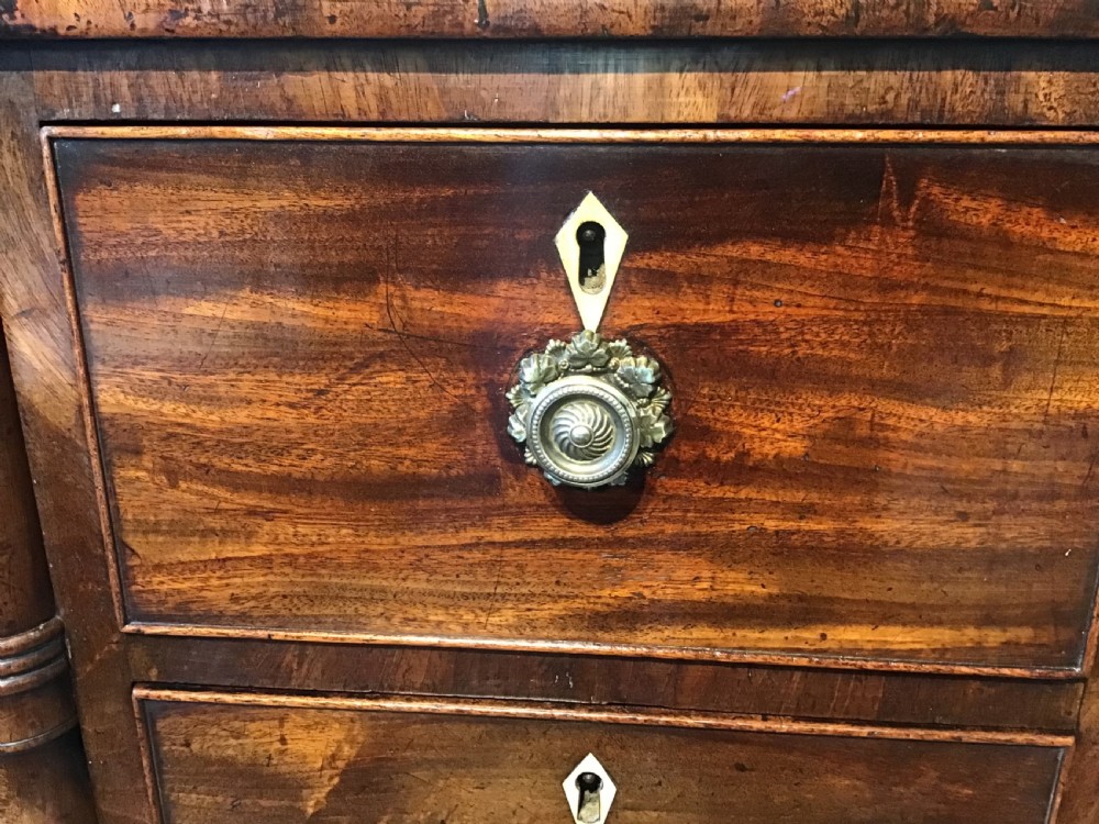 An antique Regency flame mahogany hall table featuring five drawers, brass rosette knobs, kite escutcheons, a central kneehole arch, and slim turned legs. View X