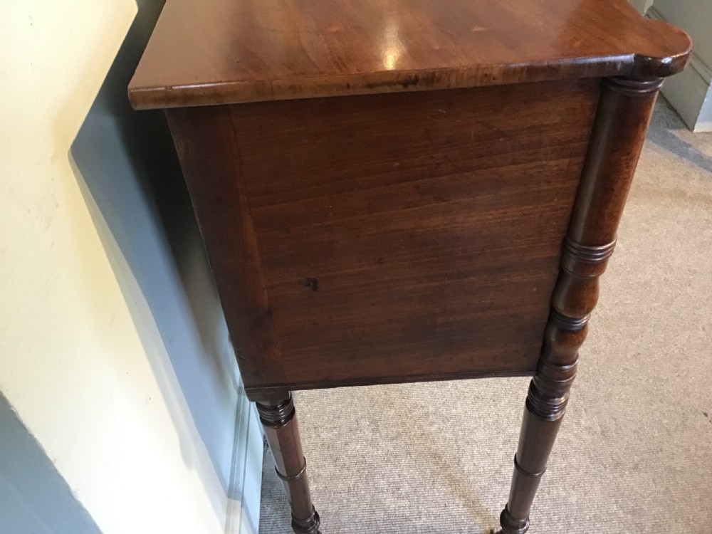 An antique Regency flame mahogany hall table featuring five drawers, brass rosette knobs, kite escutcheons, a central kneehole arch, and slim turned legs. View XII