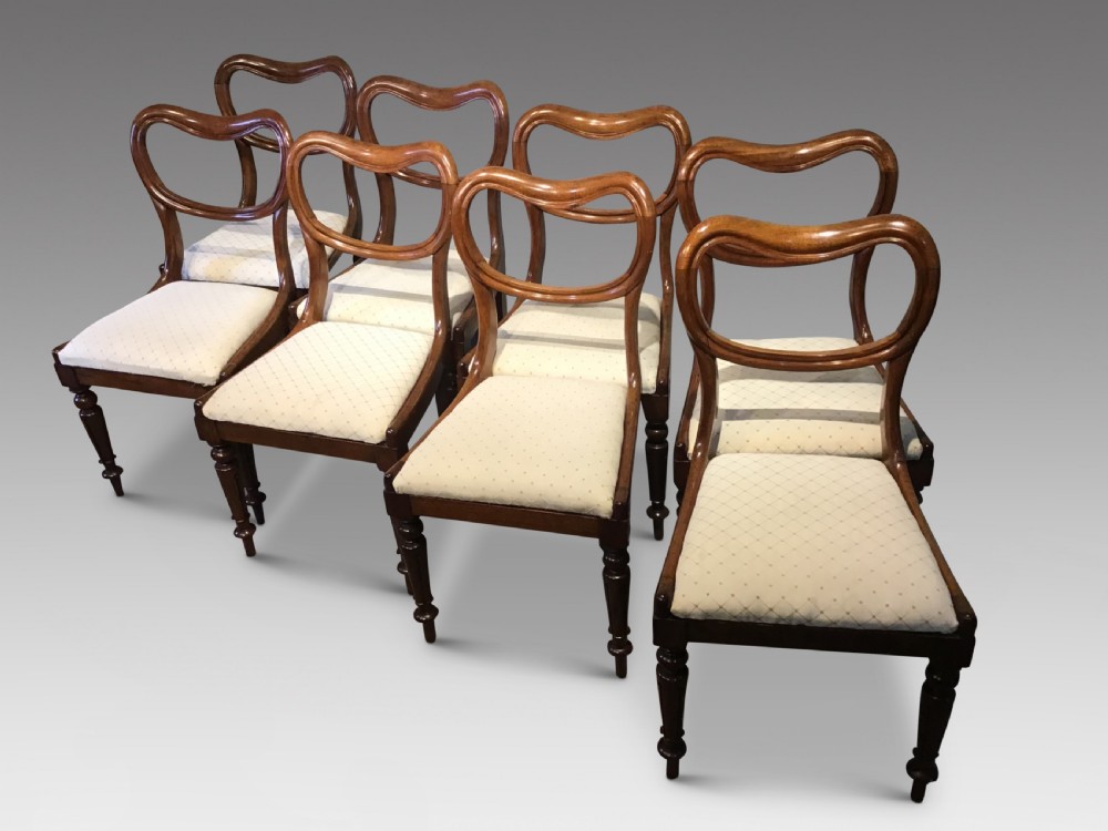 A set of eight Victorian mahogany balloon back dining chairs featuring turned front legs and light cream patterned upholstered seats.