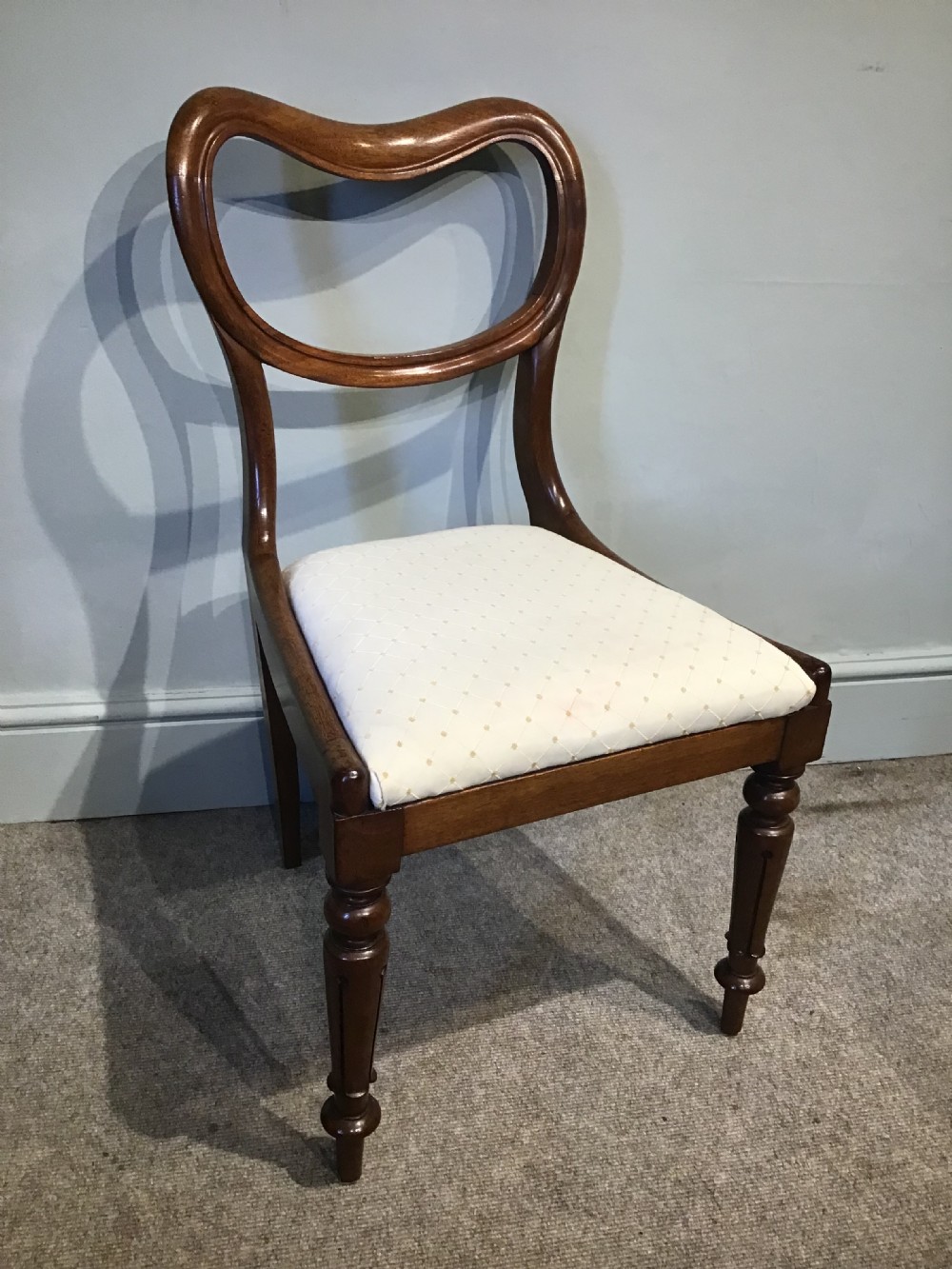A set of eight Victorian mahogany balloon back dining chairs featuring turned front legs and light cream patterned upholstered seats. View VI