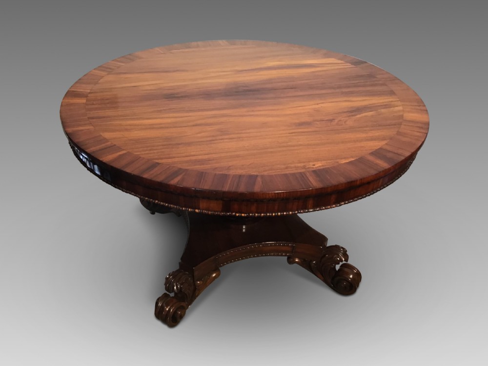 A circular antique Goncalo Alves centre table featuring a figured timber top and a pedestal base with carved scroll feet.