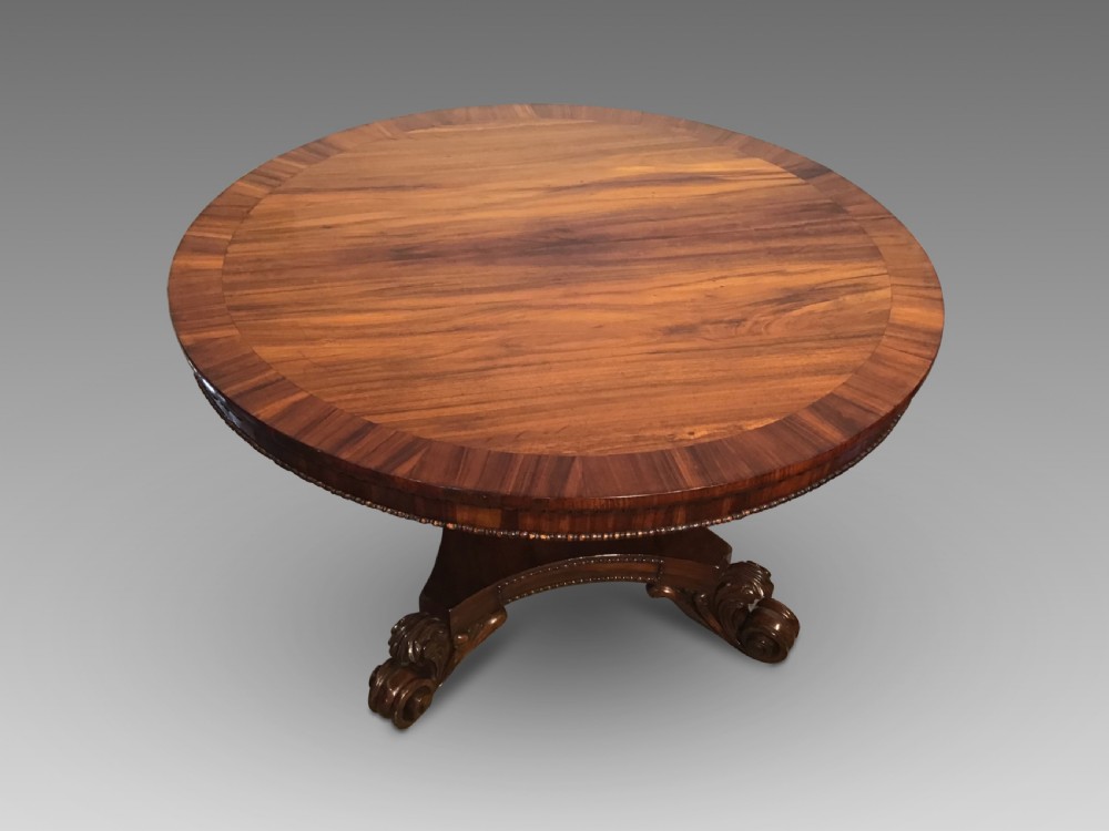 A circular antique Goncalo Alves centre table featuring a figured timber top and a pedestal base with carved scroll feet. View II
