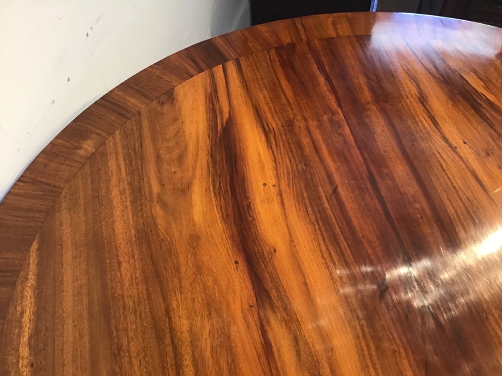 A circular antique Goncalo Alves centre table featuring a figured timber top and a pedestal base with carved scroll feet. View X