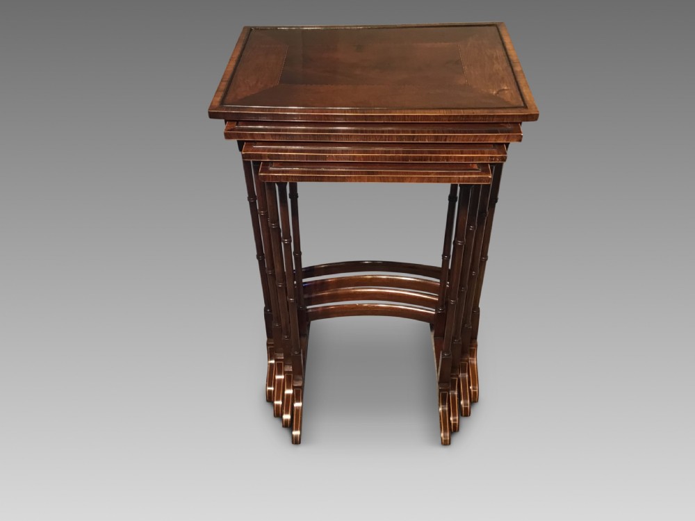 A set of four graduated dark mahogany nested tables featuring turned legs, curved rear stretchers, and splayed feet.