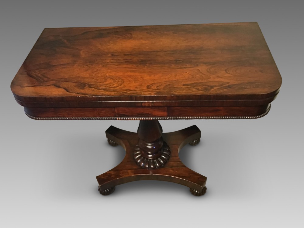 An antique rosewood fold-over card table with a beaded frieze, central turned pedestal stem, and a quadripartite plinth base on carved feet. View II