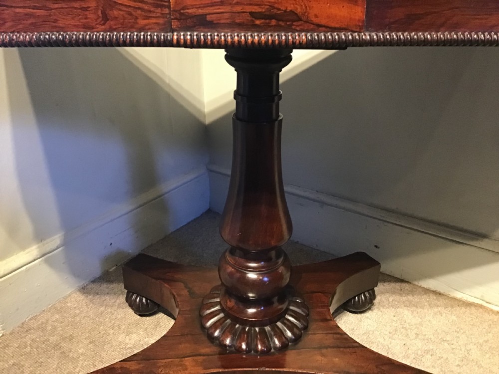 An antique rosewood fold-over card table with a beaded frieze, central turned pedestal stem, and a quadripartite plinth base on carved feet. View IV