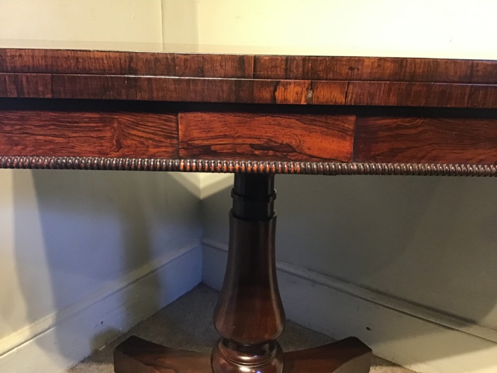 An antique rosewood fold-over card table with a beaded frieze, central turned pedestal stem, and a quadripartite plinth base on carved feet. View V