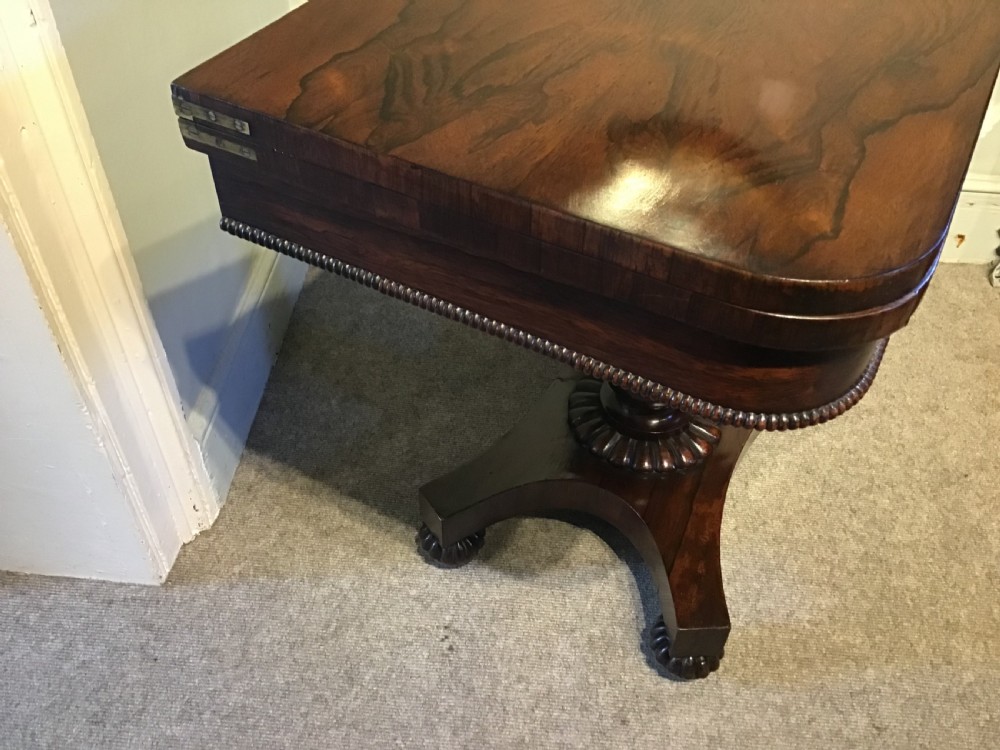An antique rosewood fold-over card table with a beaded frieze, central turned pedestal stem, and a quadripartite plinth base on carved feet. View IX