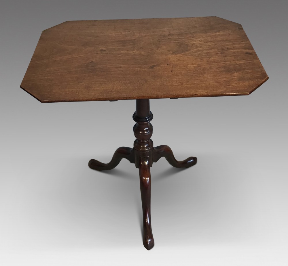 A dark mahogany Georgian tripod table with a canted rectangular top, central turned column, and three cabriole legs.