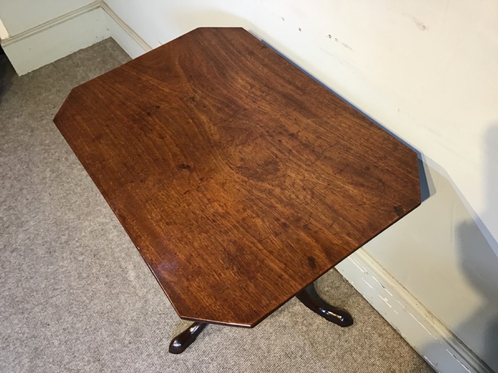 A dark mahogany Georgian tripod table with a canted rectangular top, central turned column, and three cabriole legs. View II
