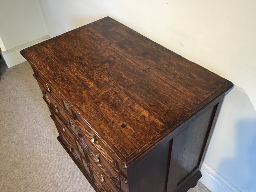 An antique dark brown oak chest featuring four drawers with geometric panel mouldings, brass teardrop handles, escutcheons, and bun feet. View III