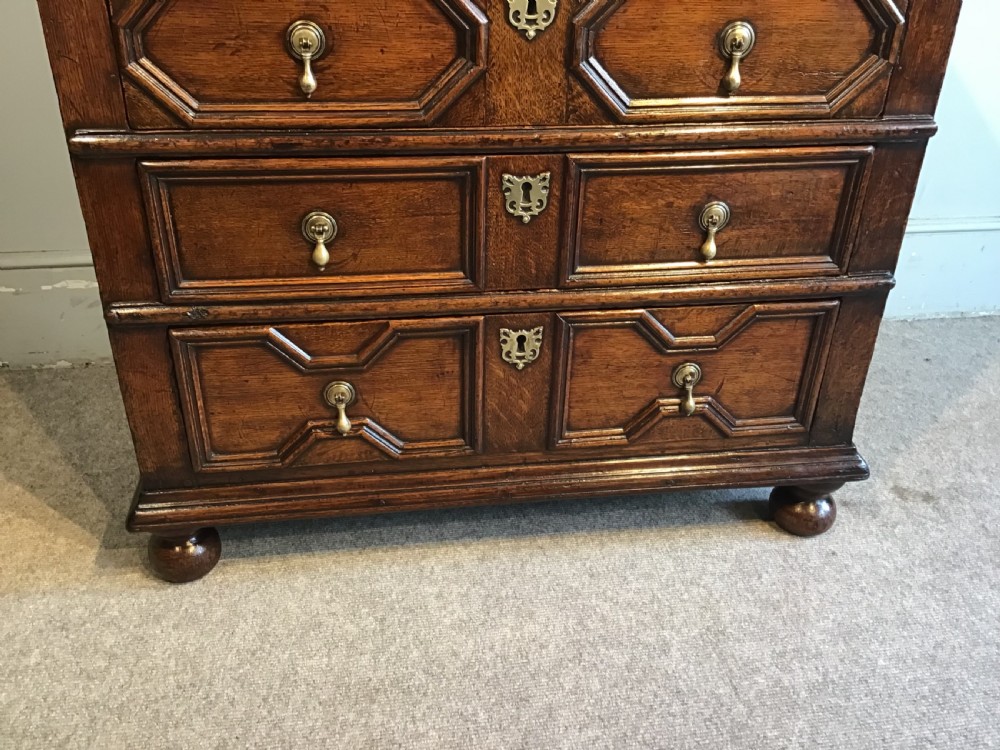 An antique dark brown oak chest featuring four drawers with geometric panel mouldings, brass teardrop handles, escutcheons, and bun feet. View VI