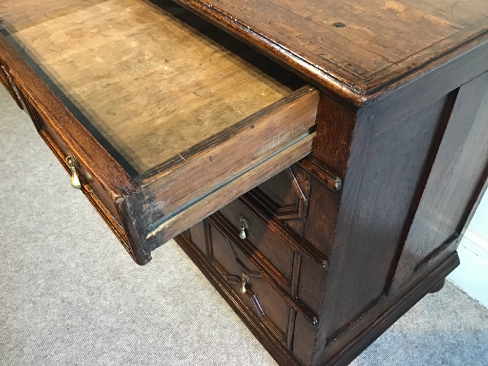 An antique dark brown oak chest featuring four drawers with geometric panel mouldings, brass teardrop handles, escutcheons, and bun feet. View VIII