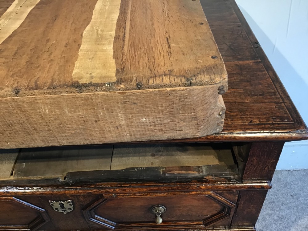 An antique dark brown oak chest featuring four drawers with geometric panel mouldings, brass teardrop handles, escutcheons, and bun feet. View X
