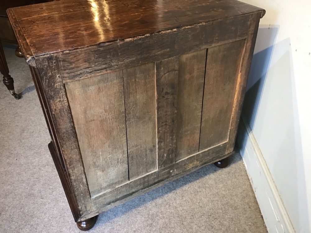 An antique dark brown oak chest featuring four drawers with geometric panel mouldings, brass teardrop handles, escutcheons, and bun feet. View XII