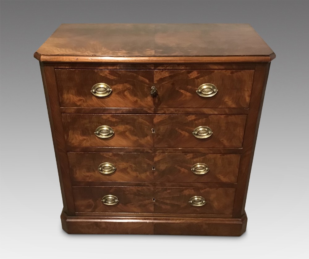 An antique flame mahogany chest of four graduated drawers featuring brass oval backplate handles and a solid plinth base.