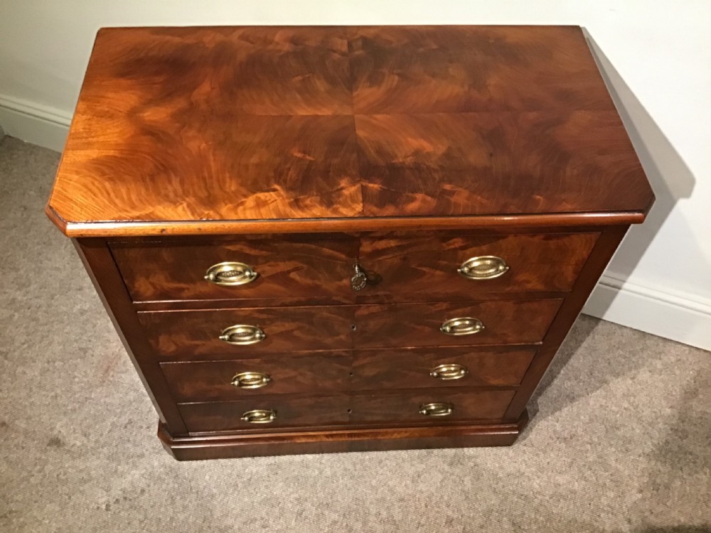 An antique flame mahogany chest of four graduated drawers featuring brass oval backplate handles and a solid plinth base. View II