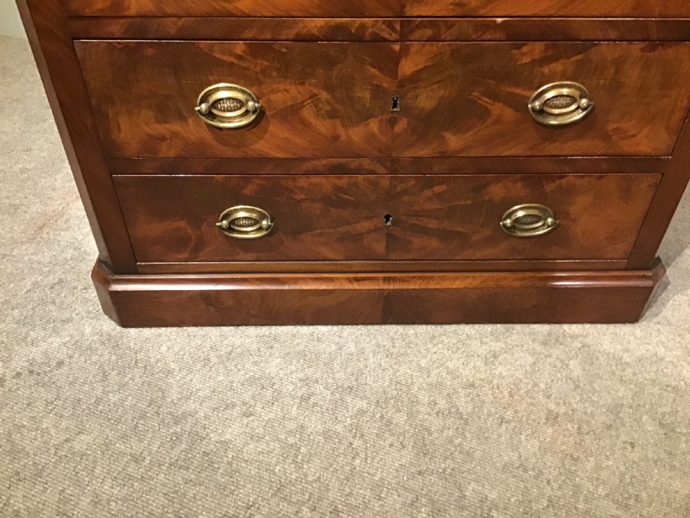 An antique flame mahogany chest of four graduated drawers featuring brass oval backplate handles and a solid plinth base. View III