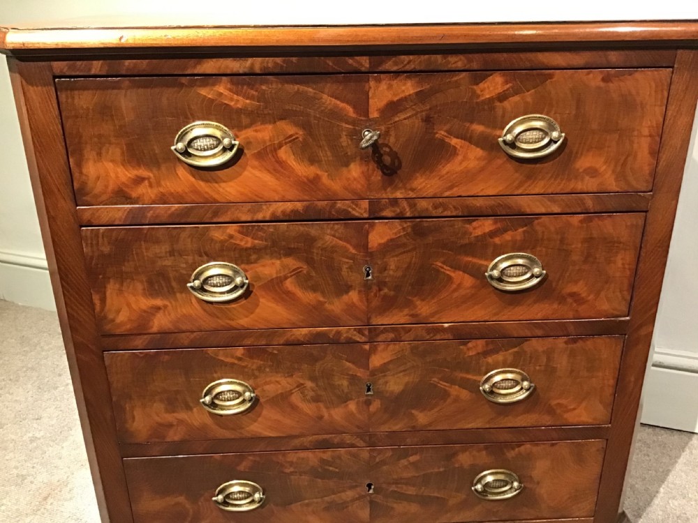An antique flame mahogany chest of four graduated drawers featuring brass oval backplate handles and a solid plinth base. View V