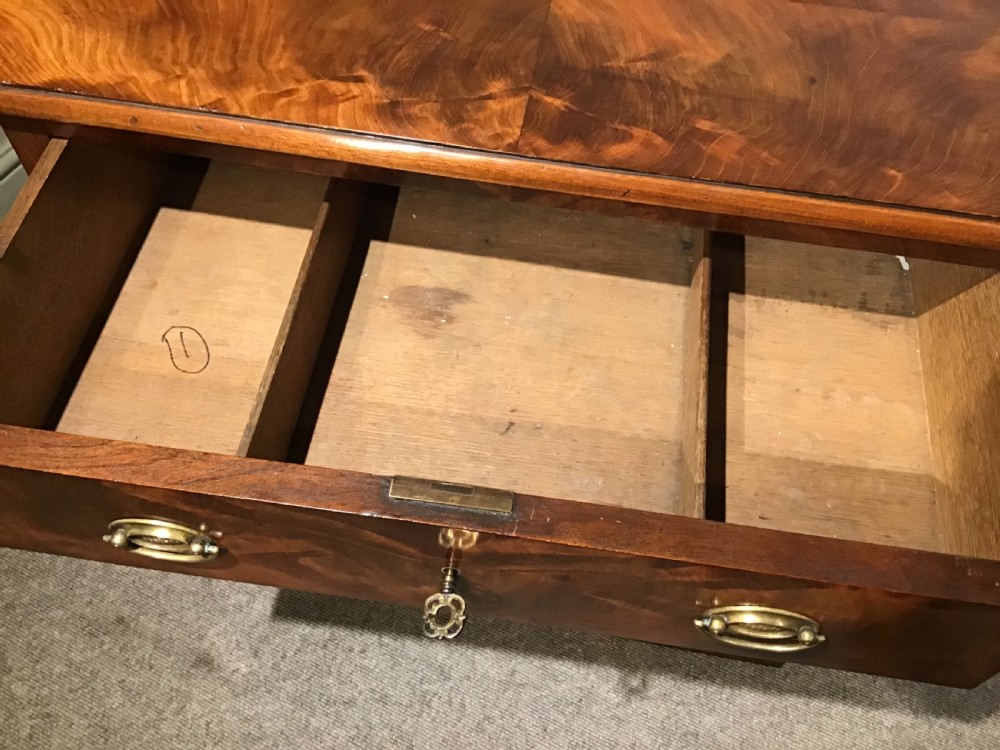 An antique flame mahogany chest of four graduated drawers featuring brass oval backplate handles and a solid plinth base. View VII