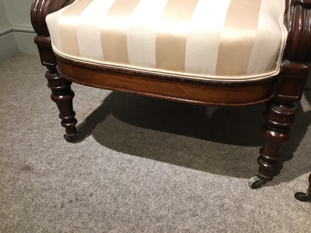 A pair of antique mahogany armchairs featuring tall arched backs, cream striped upholstery, scrolled armrests, and turned legs on castors. View V