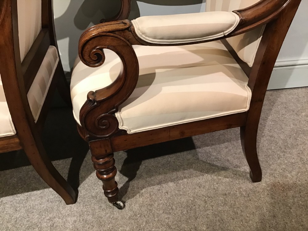 A pair of antique mahogany armchairs featuring tall arched backs, cream striped upholstery, scrolled armrests, and turned legs on castors. View X