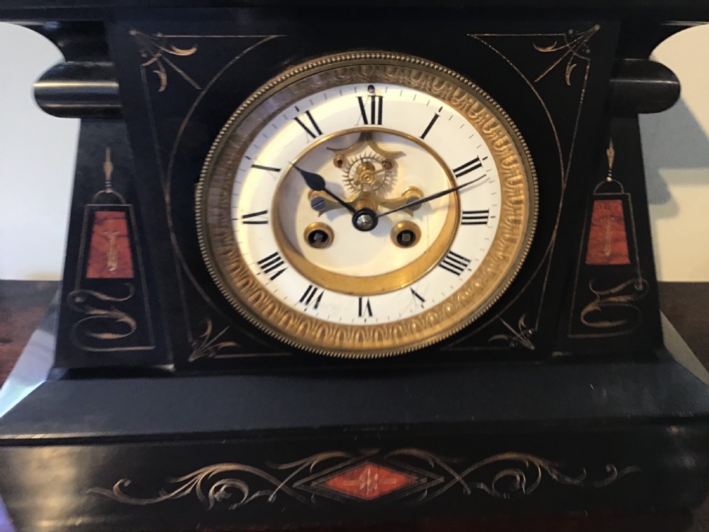 A black antique mantel clock featuring a white circular dial with Roman numerals, an exposed escapement, and gold scrollwork detailing across the case. View III