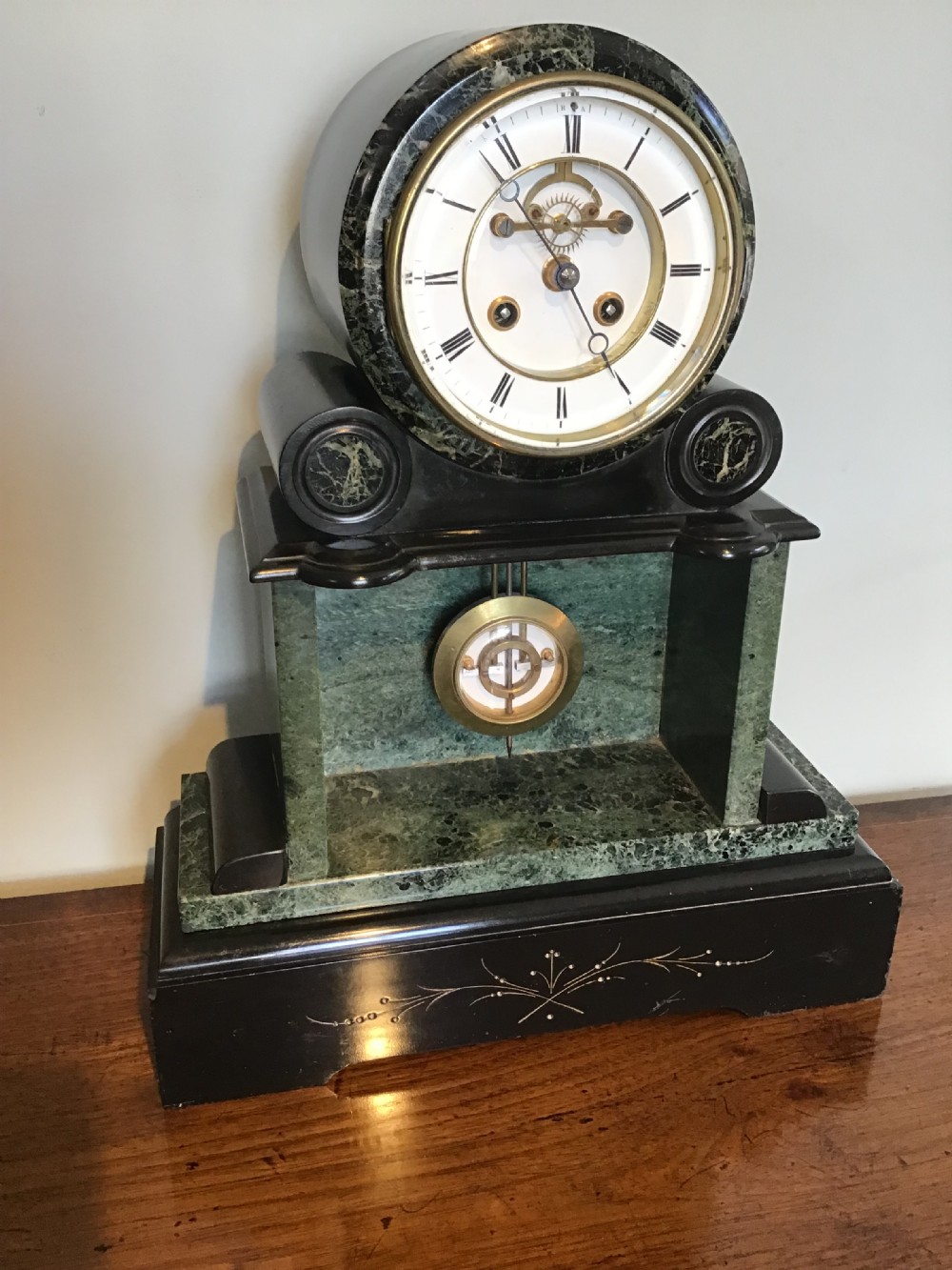 A Victorian black slate and green marble mantel clock featuring a white dial with a visible escapement and a brass pendulum.