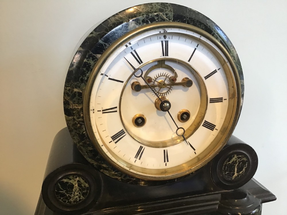 A Victorian black slate and green marble mantel clock featuring a white dial with a visible escapement and a brass pendulum. View II