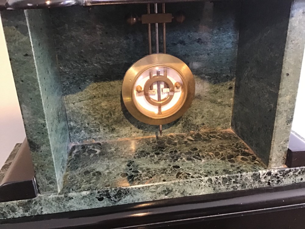 A Victorian black slate and green marble mantel clock featuring a white dial with a visible escapement and a brass pendulum. View III