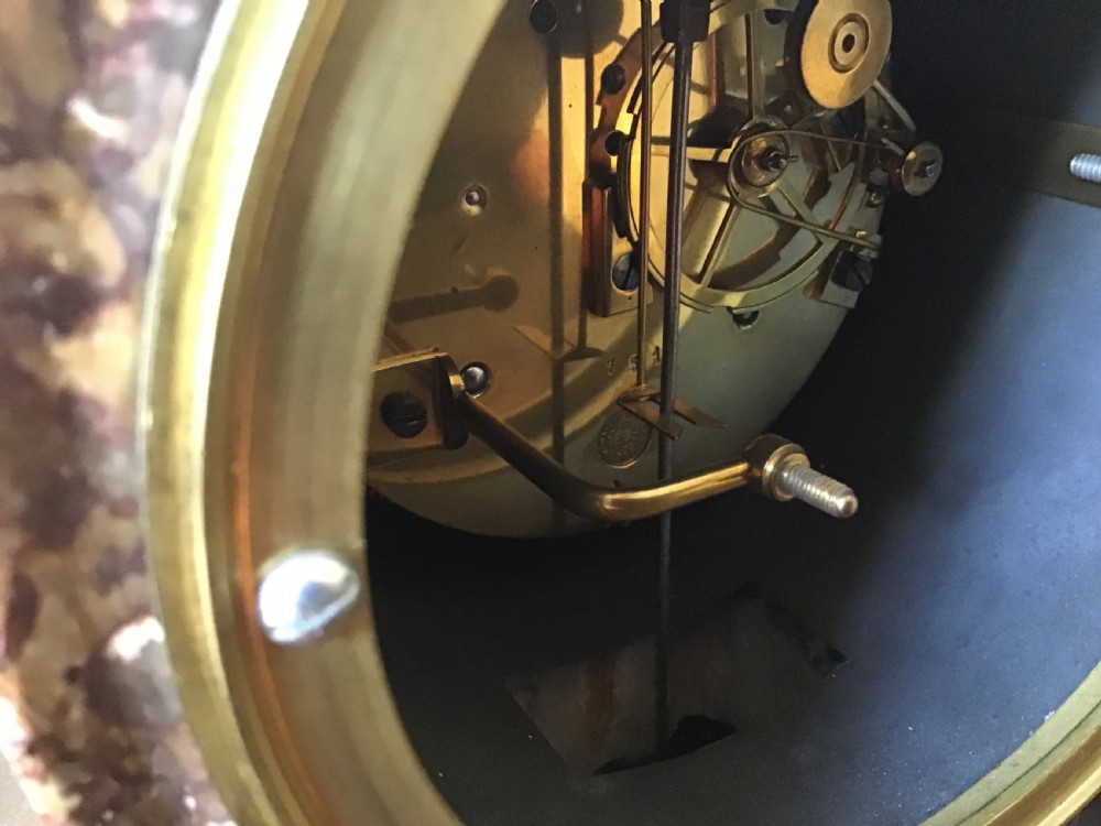 A Victorian black slate and variegated marble drumhead mantel clock featuring a brass-rimmed circular dial set above a scrolled architectural base. View VII