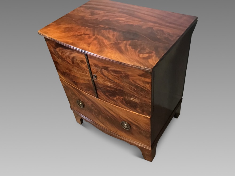 An antique bowfront cabinet crafted from flame mahogany veneer with two upper cupboard doors, a lower drawer with round brass ring pulls, and bracket feet. View II
