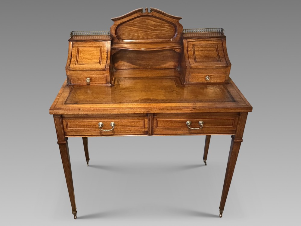 An antique mahogany writing desk featuring a central leather surface, a raised superstructure with stationery compartments, two frieze drawers, and tapered legs on brass castors.