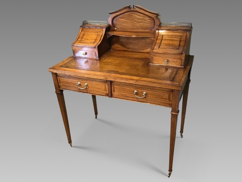 An antique mahogany writing desk featuring a central leather surface, a raised superstructure with stationery compartments, two frieze drawers, and tapered legs on brass castors. View II