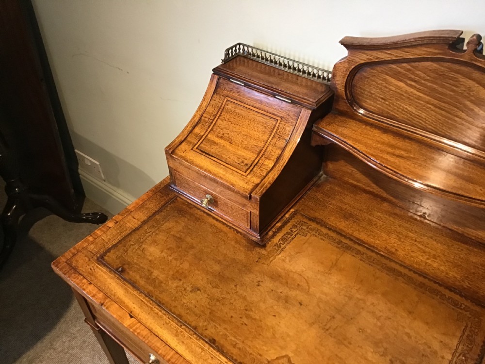 An antique mahogany writing desk featuring a central leather surface, a raised superstructure with stationery compartments, two frieze drawers, and tapered legs on brass castors. View III