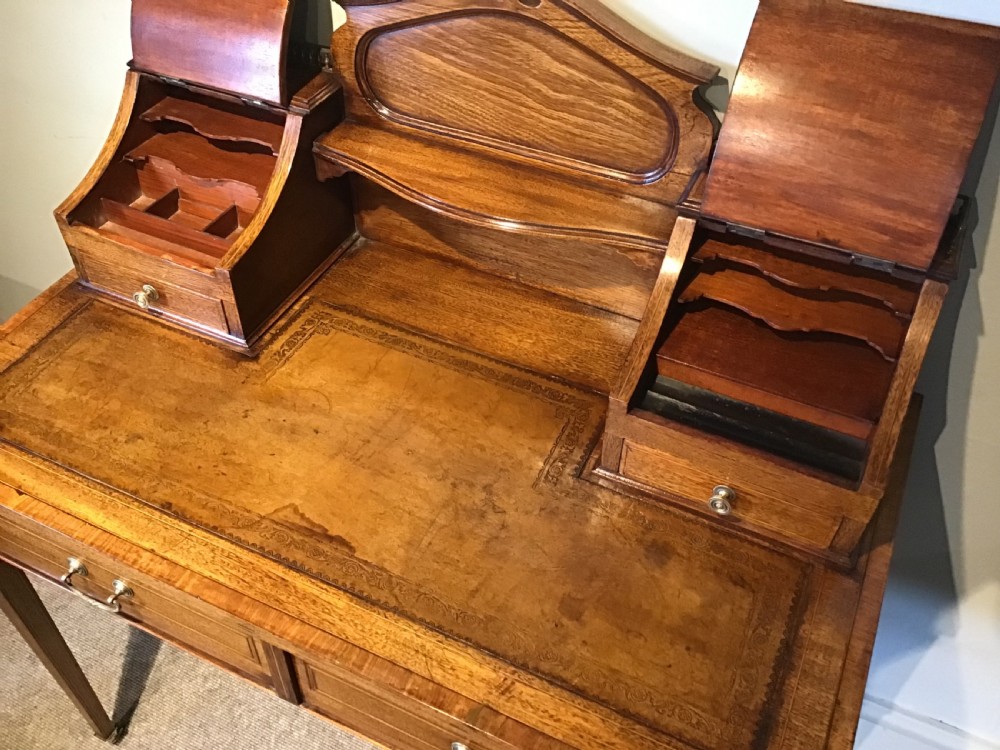 An antique mahogany writing desk featuring a central leather surface, a raised superstructure with stationery compartments, two frieze drawers, and tapered legs on brass castors. View IV