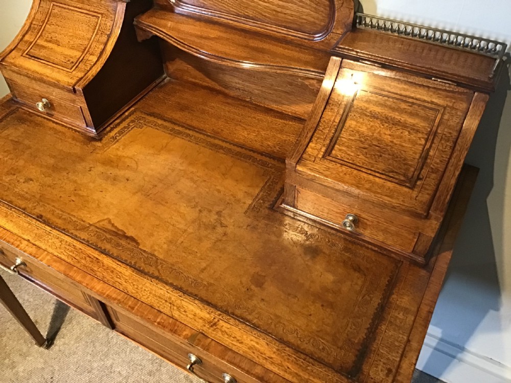 An antique mahogany writing desk featuring a central leather surface, a raised superstructure with stationery compartments, two frieze drawers, and tapered legs on brass castors. View V