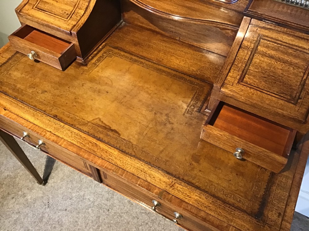 An antique mahogany writing desk featuring a central leather surface, a raised superstructure with stationery compartments, two frieze drawers, and tapered legs on brass castors. View VI