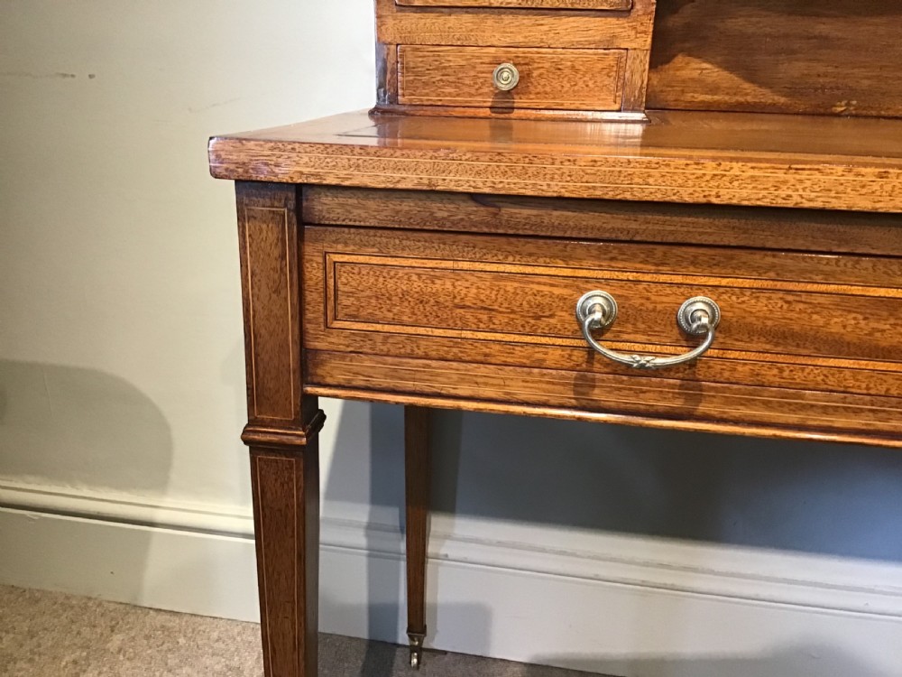 An antique mahogany writing desk featuring a central leather surface, a raised superstructure with stationery compartments, two frieze drawers, and tapered legs on brass castors. View VII